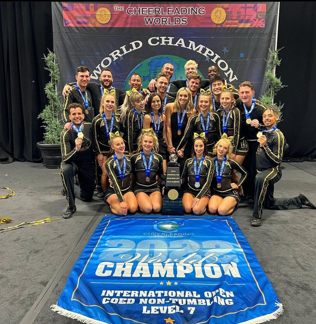 Male and female cheerleading. Wearing gold medals and with a banner that says World champion. The cheerleader have big smile